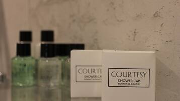 A bathroom with a marble wall, two green bottles, and two white boxes labeled 'COURTESY SHOWER CAP' and 'COURTESY SHOWER CREAM'.