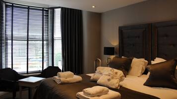 A hotel room with a large bed, a desk, and a chair. There are towels on the bed and a lamp on the desk.