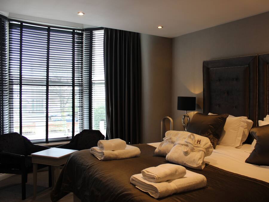 A hotel room with a large bed, a desk, and a chair. There are towels on the bed and a lamp on the desk.