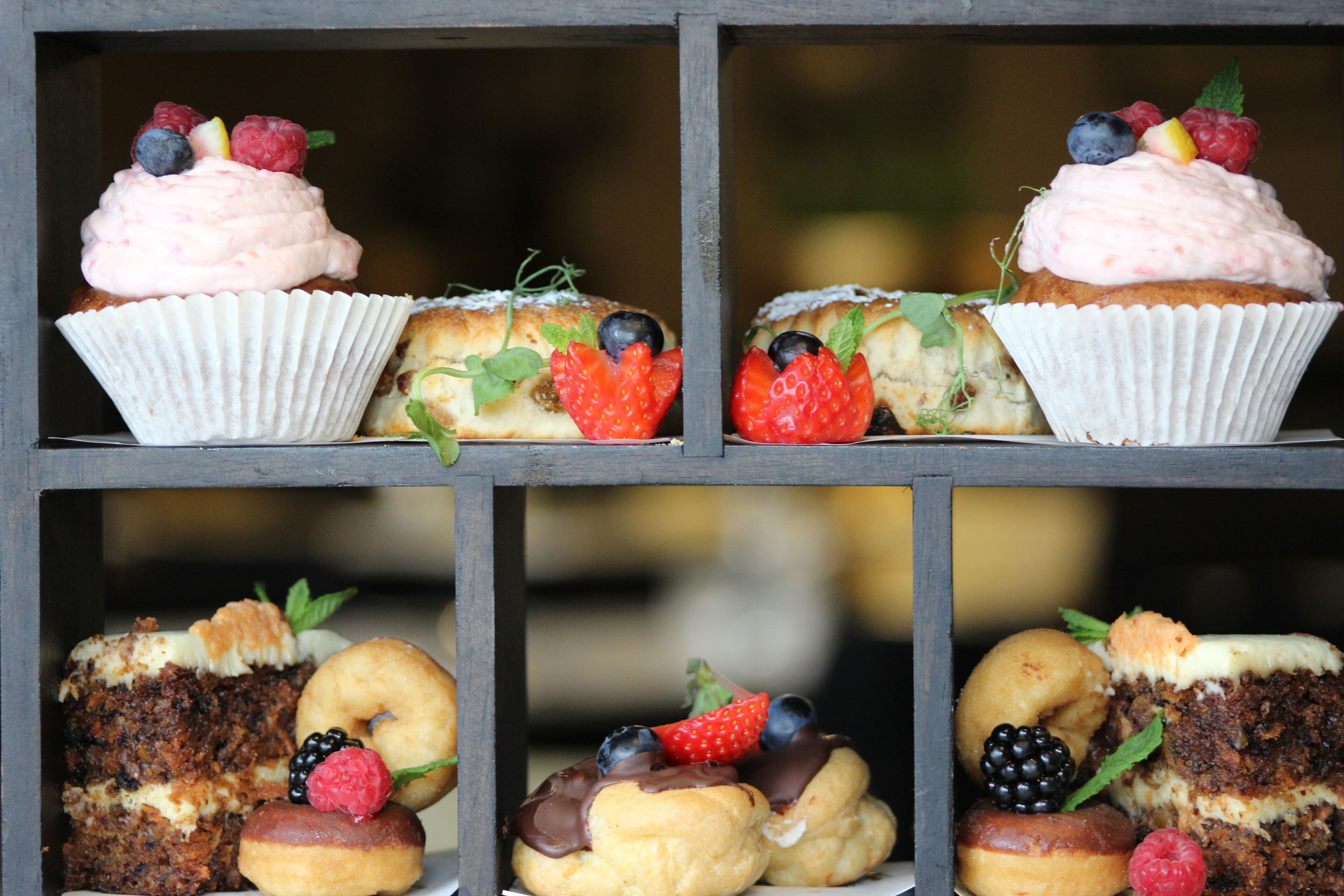 Uma mesa de sobremesas com diversos doces e bolos, incluindo cupcakes e donuts, cobertos com frutas e creme.