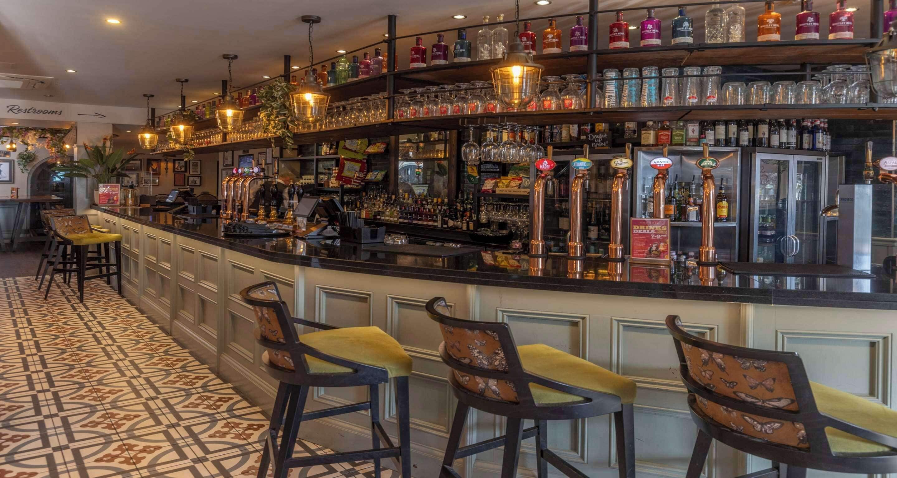 A bar area with stools, a counter, and shelves stocked with bottles.