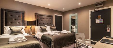 A hotel room with two beds, a desk, a chair, and a door with a security camera.