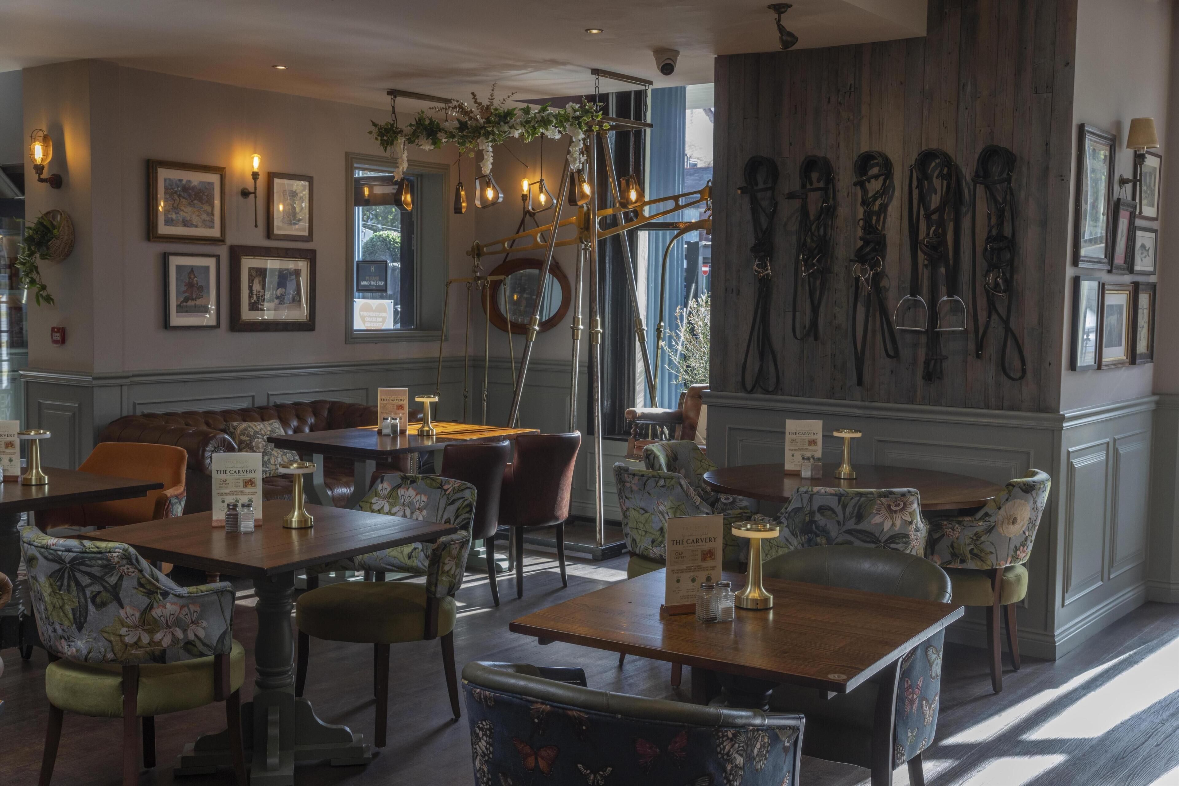A restaurant with wooden tables, leather chairs, and a wall-mounted horse tack display.
