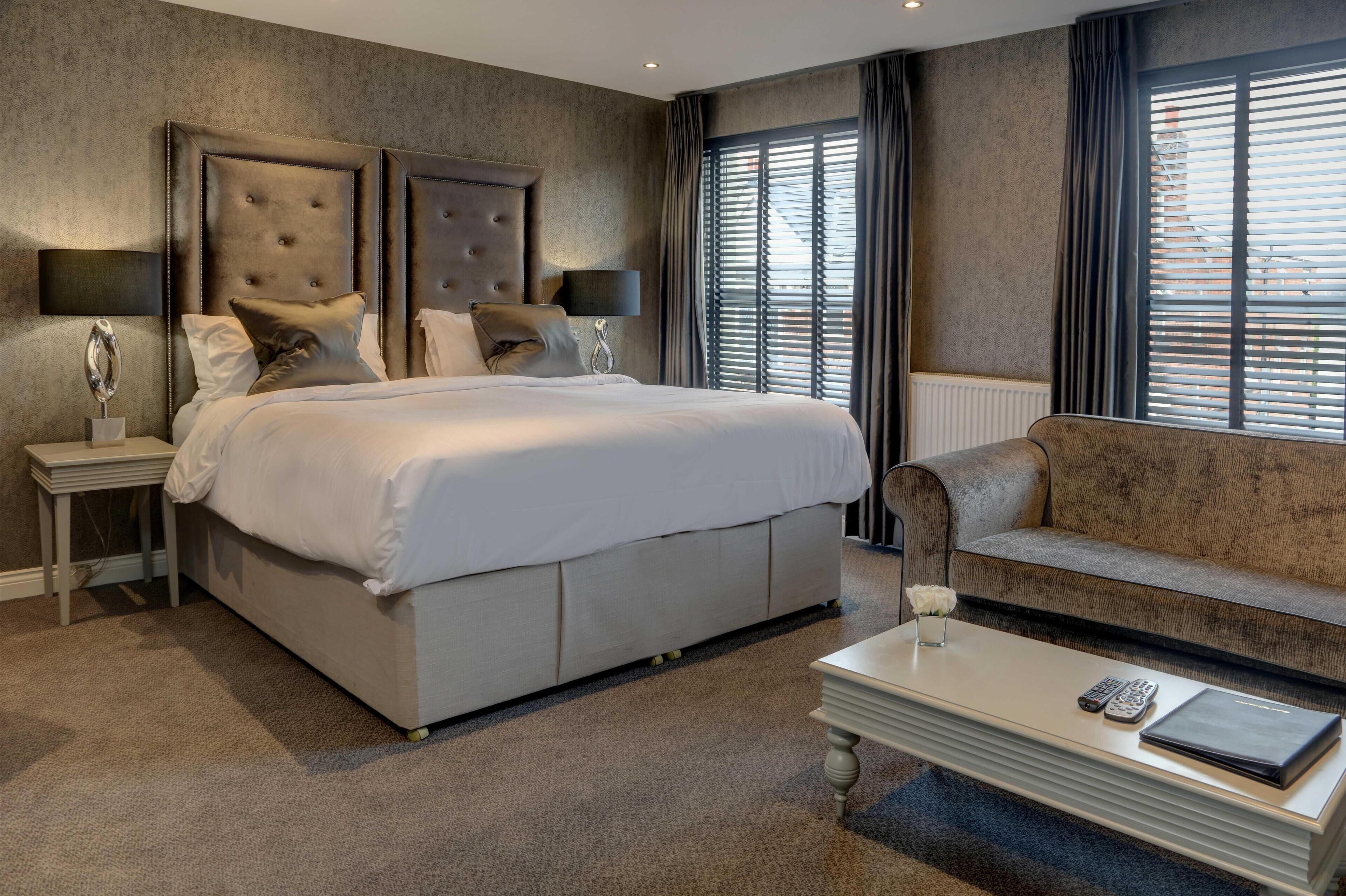 A bedroom with a large bed, a sofa, a coffee table, and a window with blinds.