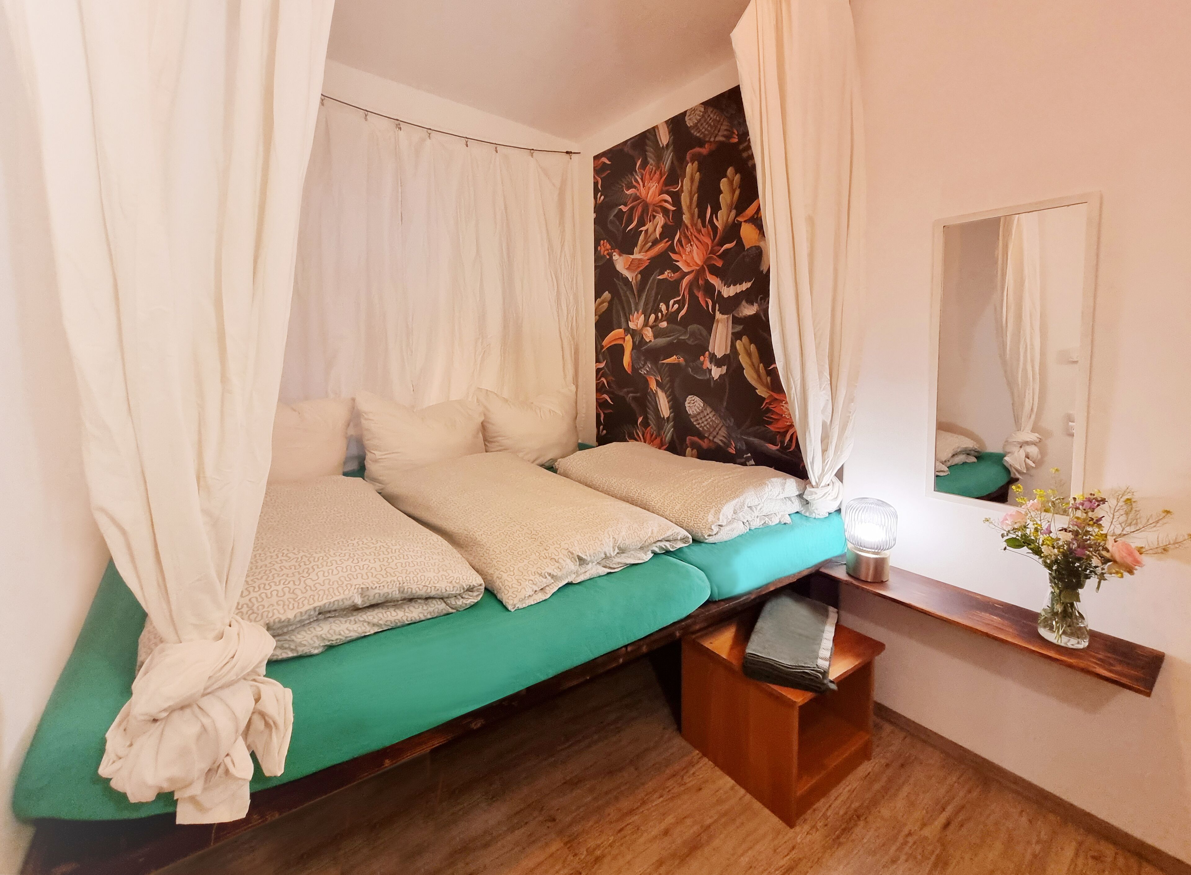 A room with a bed, a bedside table, a mirror, and a curtain.