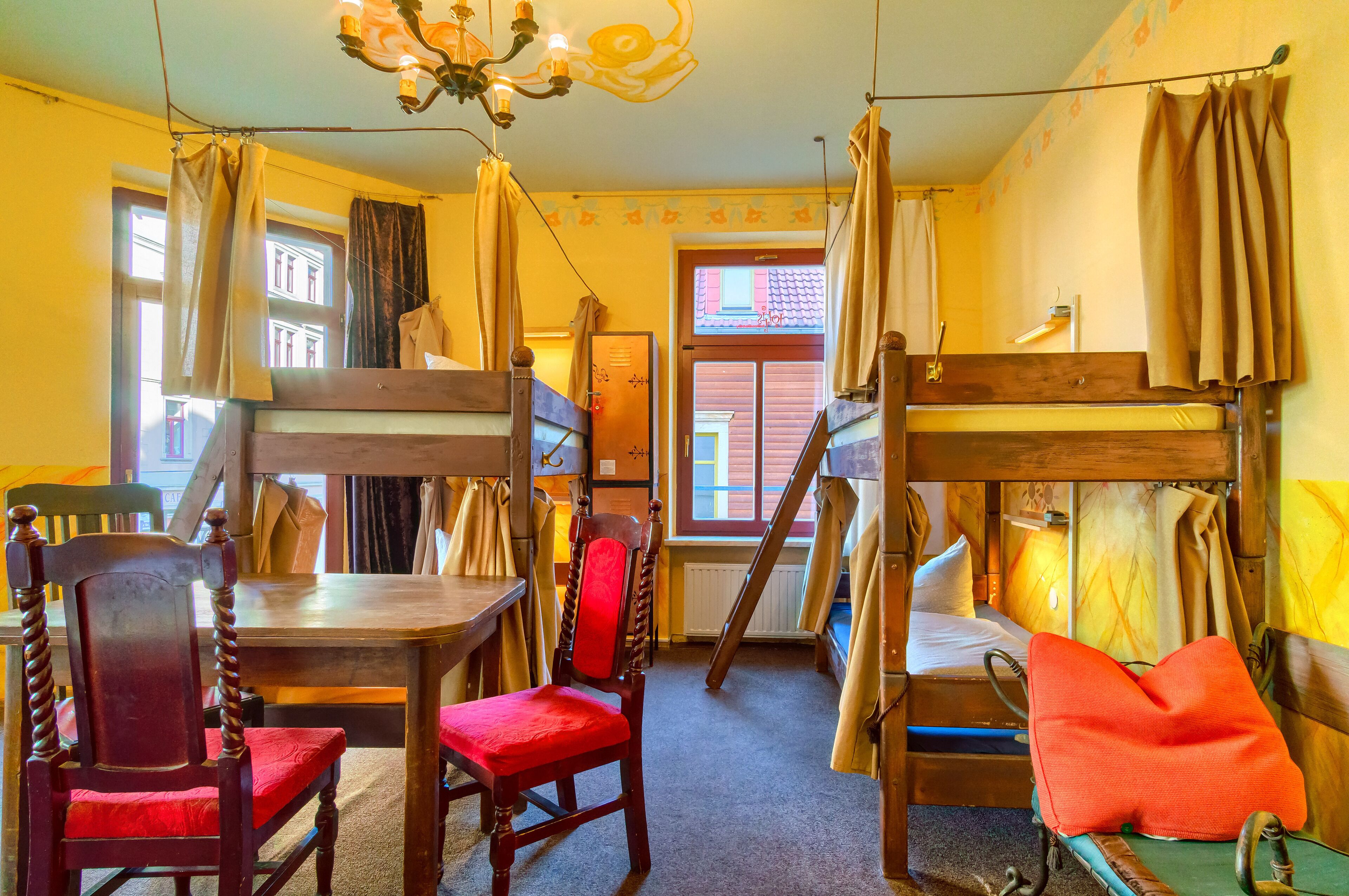 Ein Zimmer mit Stockbetten, einem Holztisch, Stühlen und einer Kandelaber.