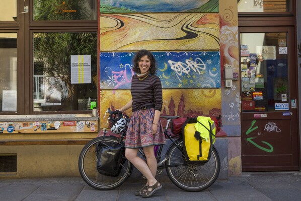 A person standing next to a bicycle with a yellow bag, in front of a colorful mural and a building entrance. - Lollis Homestay - Hostel (Dresden)