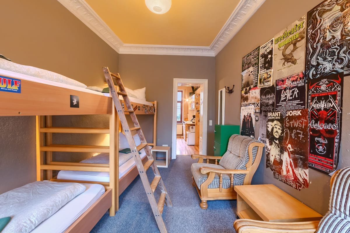 A room with bunk beds, a ladder, a chair, and posters on the wall.