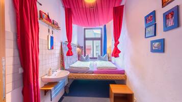 Una habitación pequeña e iluminada con una cama, un lavamanos y una ventana.