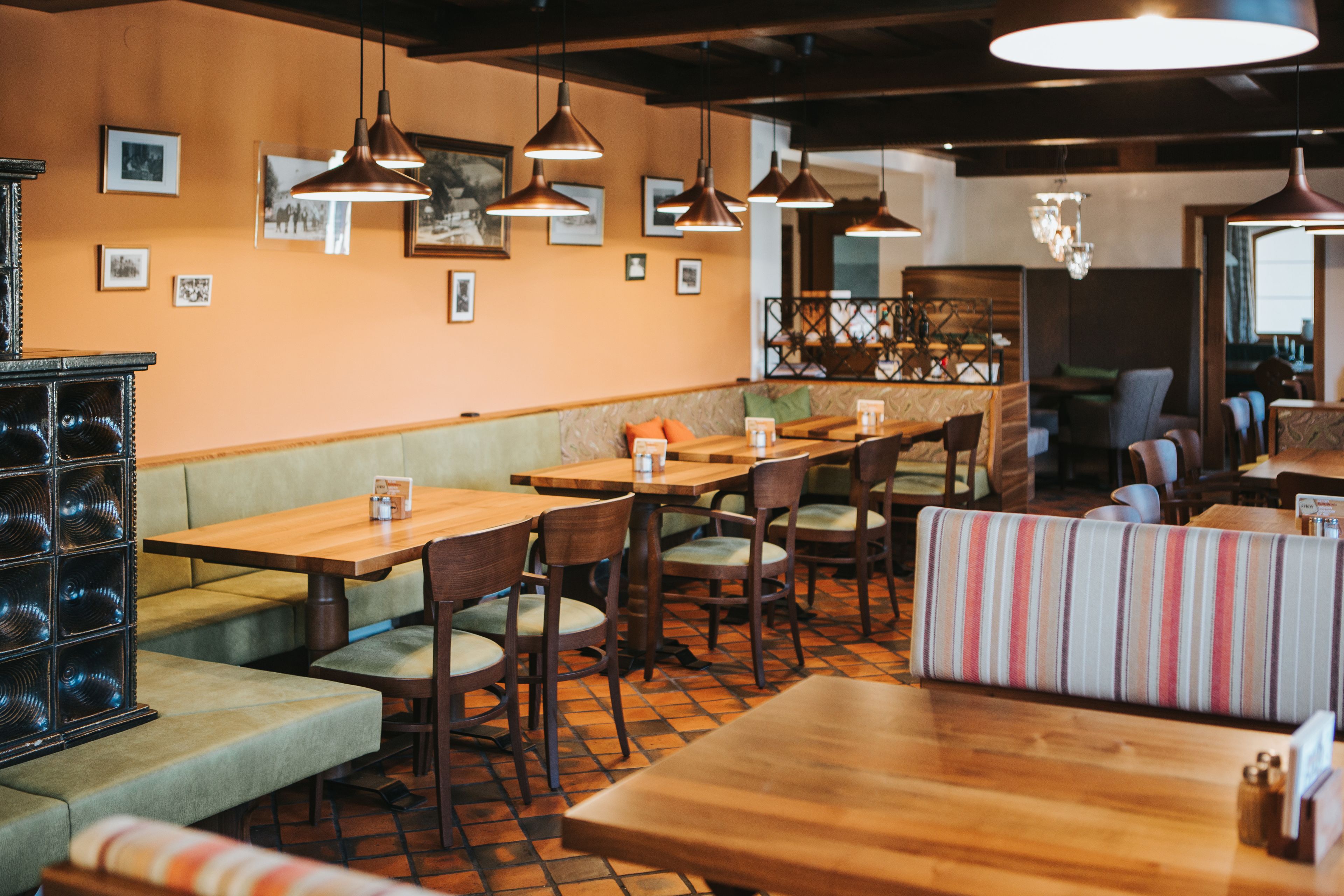Un interior de restaurante con mesas y cabinas de madera, lámparas colgantes y cuadros en las paredes.
