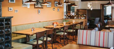 Un interior de restaurante con mesas y cabinas de madera, lámparas colgantes y cuadros en las paredes.
