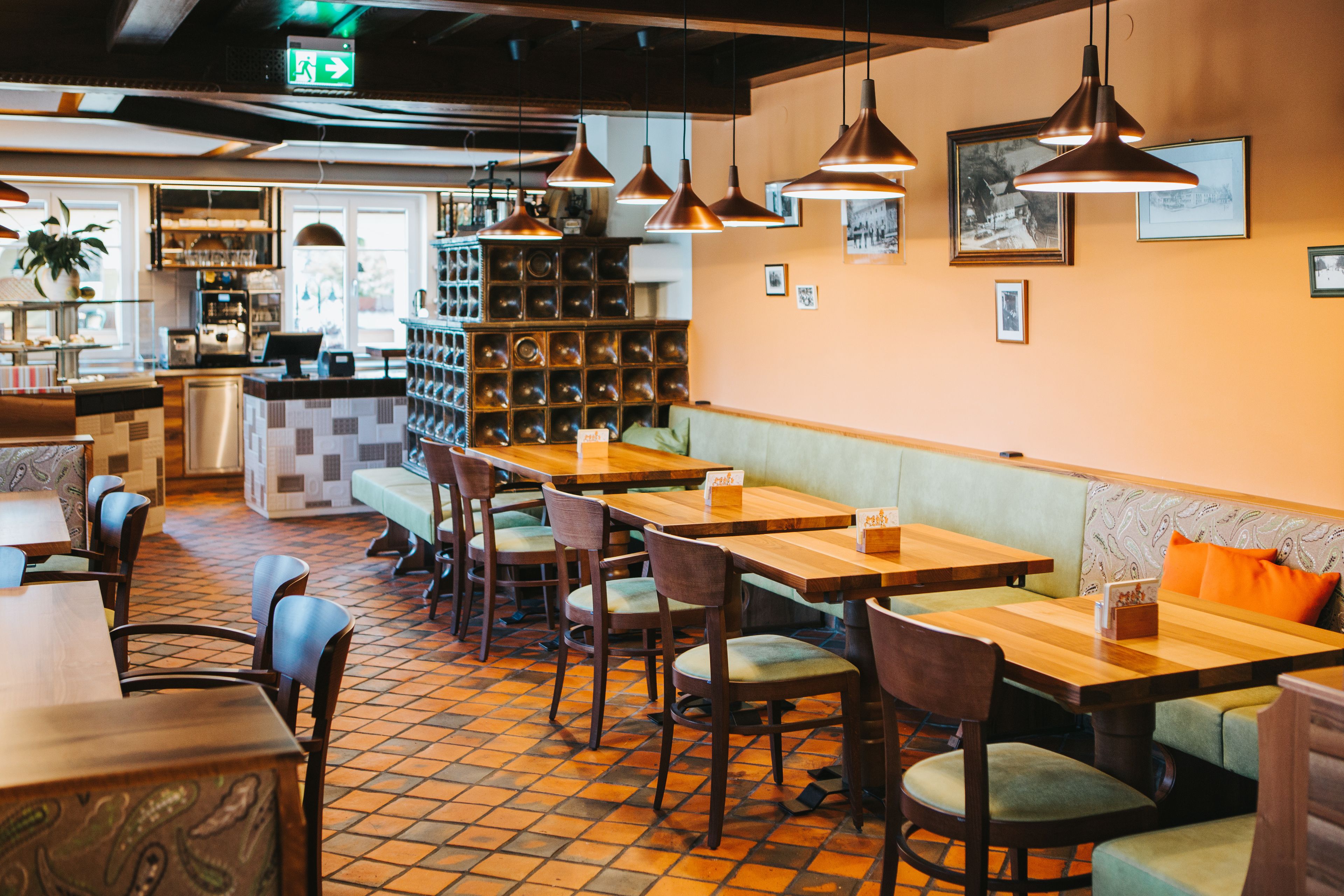 L’intérieur d’un restaurant est aménagé avec des tables et des chaises en bois, un comptoir et un espace détente avec des coussins à motifs.