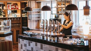 Un'area bar con un bancone, scaffali con bottiglie e luci a sospensione.