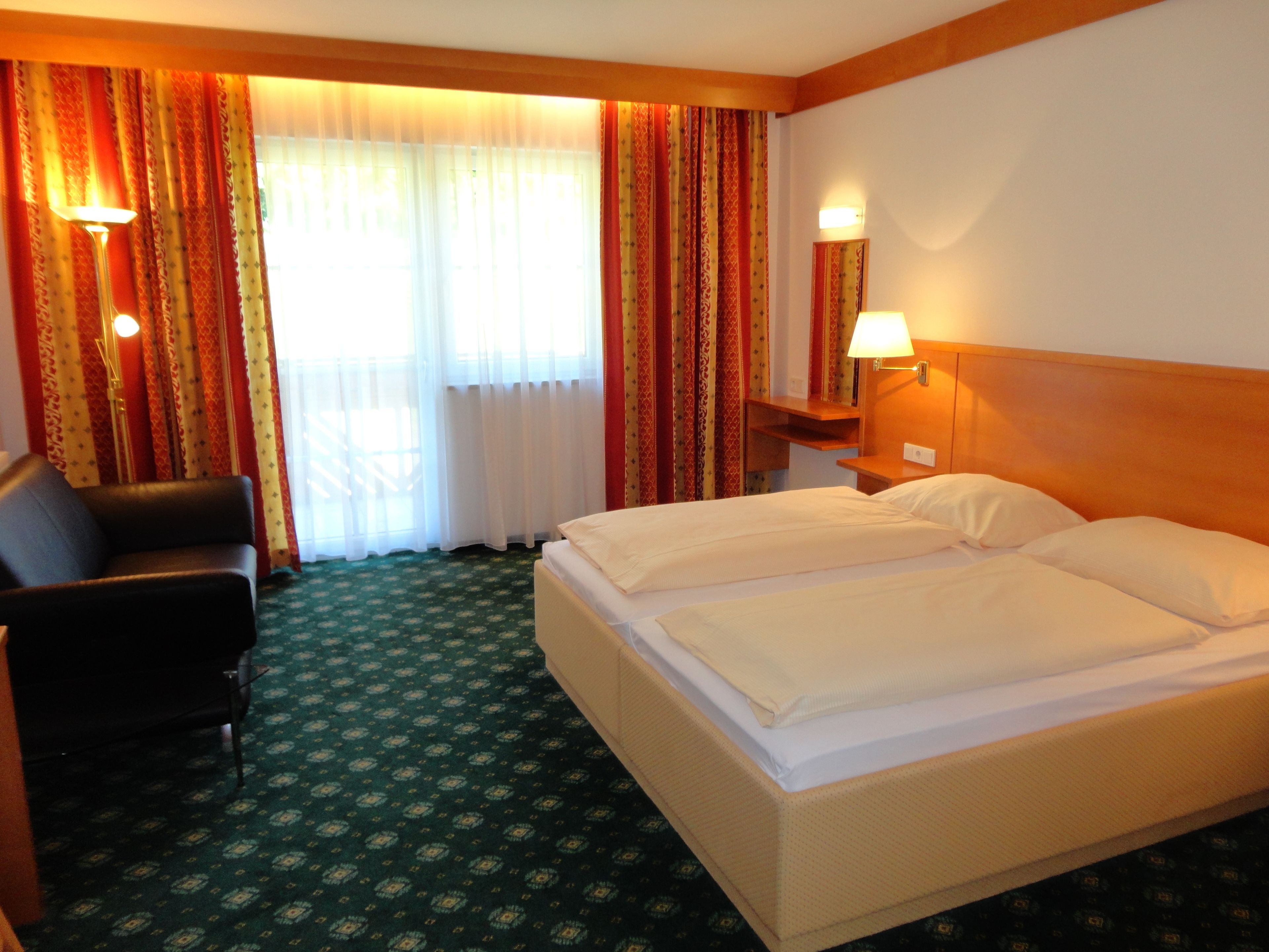 A hotel room with a bed, a chair, a nightstand with a lamp, and curtains.
