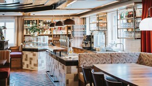 Interno di un ristorante con pavimento piastrellato, area bar con bottiglie e bicchieri, e zona salotto con cuscini decorati.