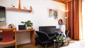 A hotel room with a desk, a black leather sofa, a glass coffee table, and a bed.