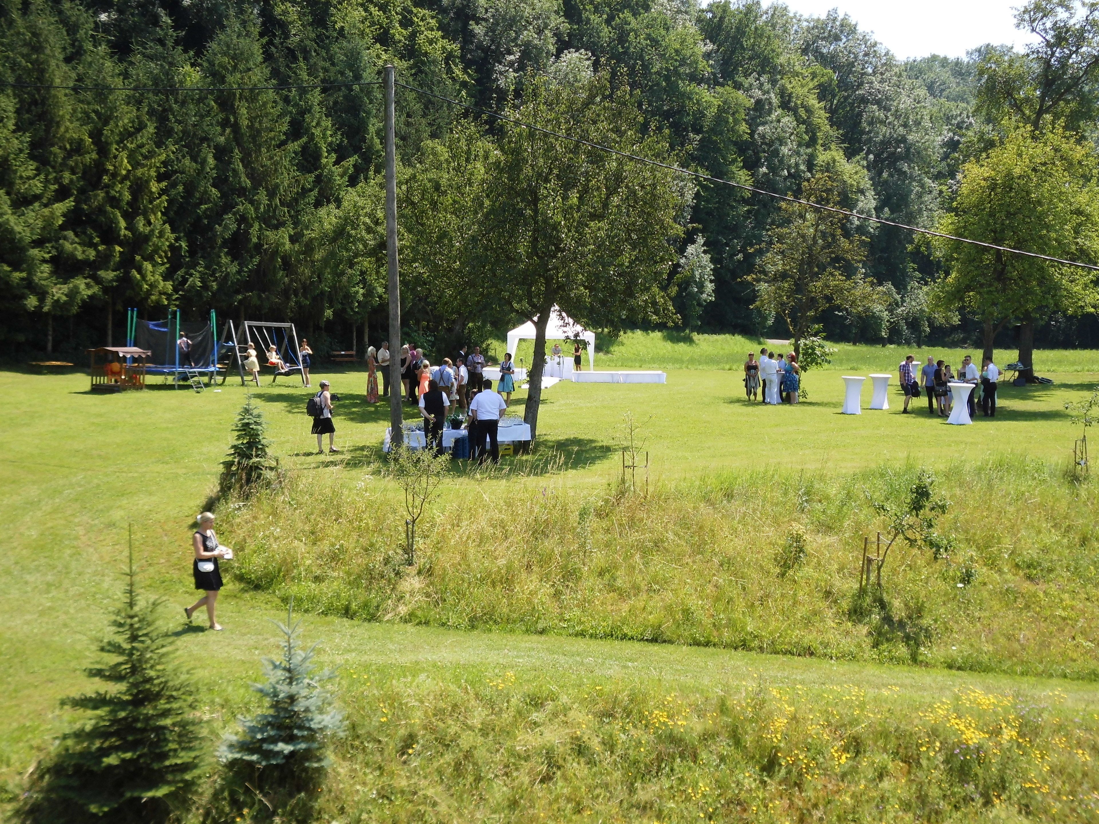 A grassy outdoor area with a stage and tables, surrounded by trees.