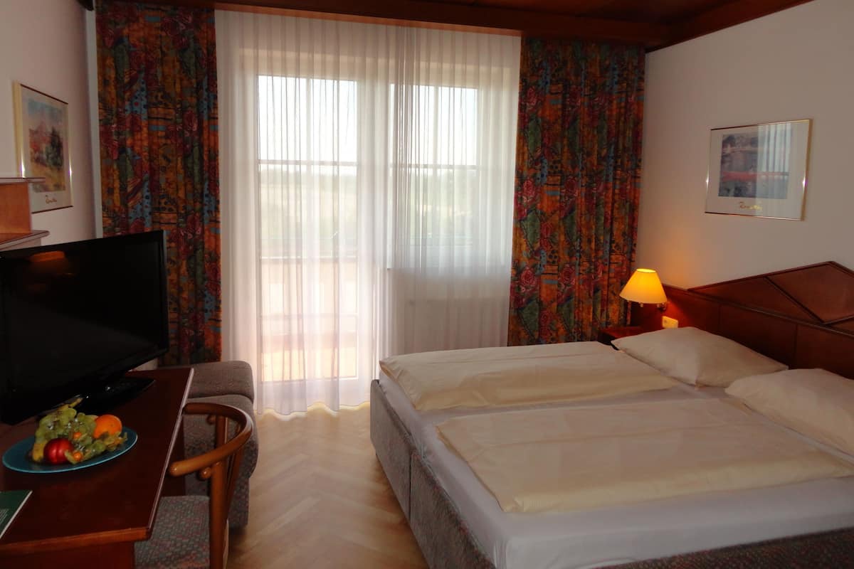 A hotel room with a bed, a desk with a television, a chair, a lamp, and a window with curtains.