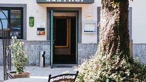 Un edificio con insegna "GASTHOF", una porta, un albero di fronte e tavoli e sedie all'aperto.