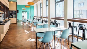 A modern restaurant with wooden flooring, teal walls, and large windows offering city views. Tables and chairs are arranged for dining. - B&B Hotel Graz-Hbf (Graz)