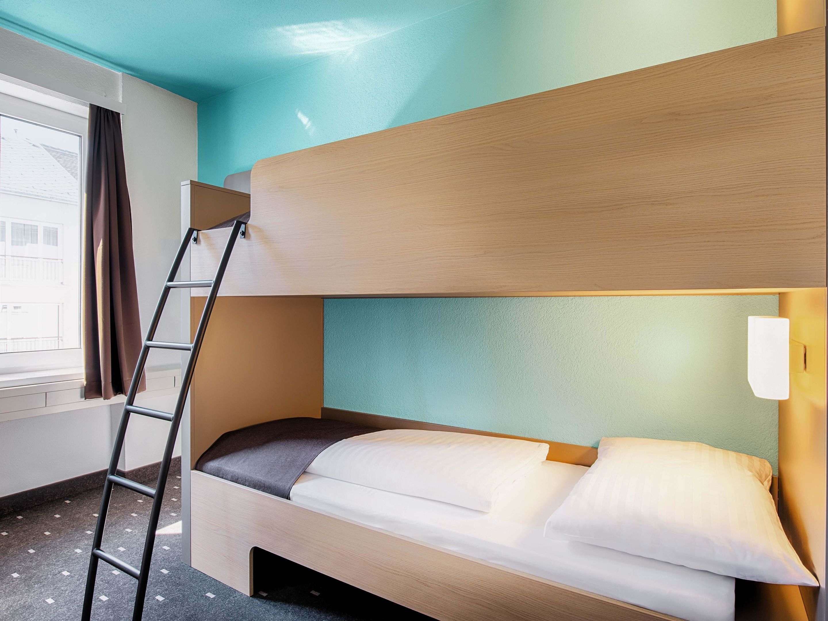 Ein Stockbett mit einer Leiter, ein Fenster mit Vorhängen und eine Wandleuchte.
