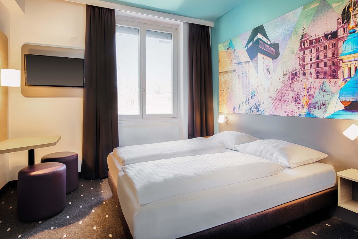 A hotel room with a bed, a desk, and a large window.