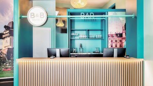 Un espace bar aux couleurs turquoise, une enseigne B&B Hotels et un comptoir avec des verres et une machine à café.