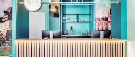 Zona de bar con decoración en tonos turquesa, un cartel de B&B Hotels y una barra con vasos y una cafetera.