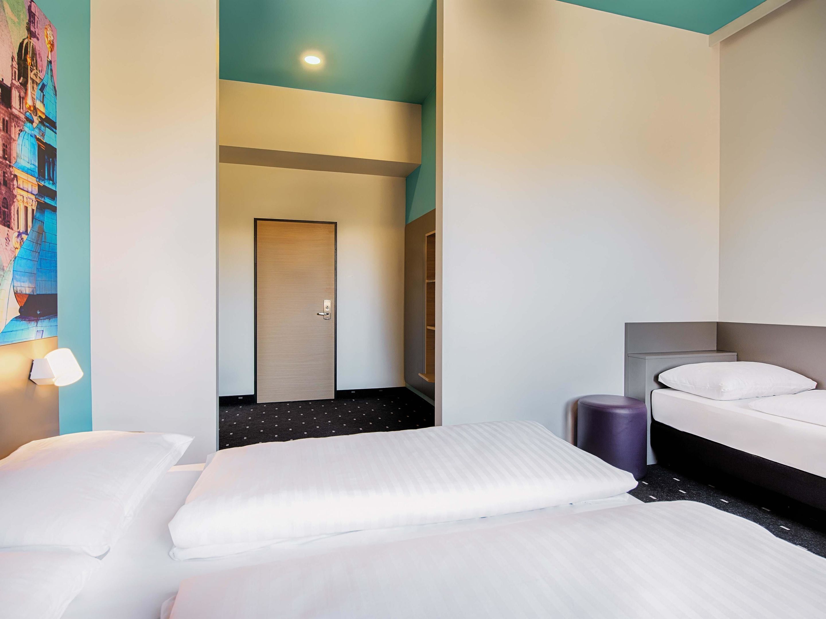 Una habitación de hotel con cama, mesita de noche y puerta.