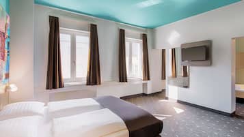 A hotel room with two beds, a large window with curtains, a flat-screen TV mounted on the wall, and a patterned floor.