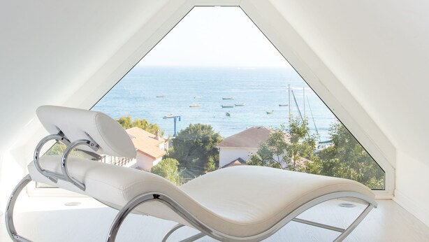 Una habitación moderna con una mecedora blanca, techo inclinado y vista al mar.