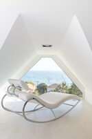 Una habitación moderna con una mecedora blanca, techo inclinado y vista al mar.