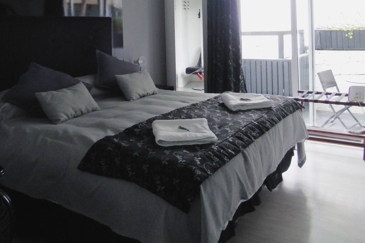 A modern hotel room with a large bed, a flat-screen TV, and a balcony with a chair.
