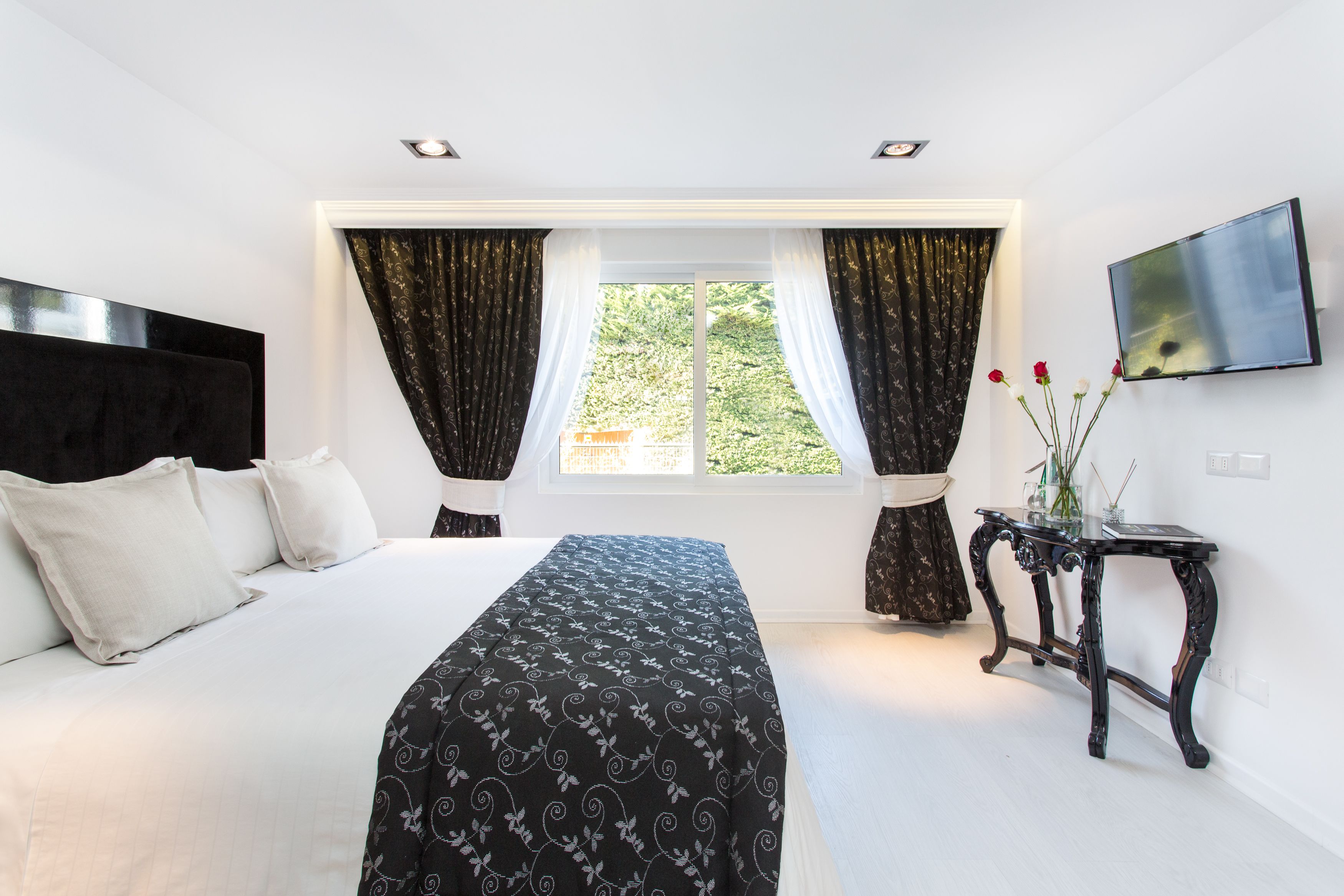 A bedroom with a bed, curtains, a TV, and a window with a view.