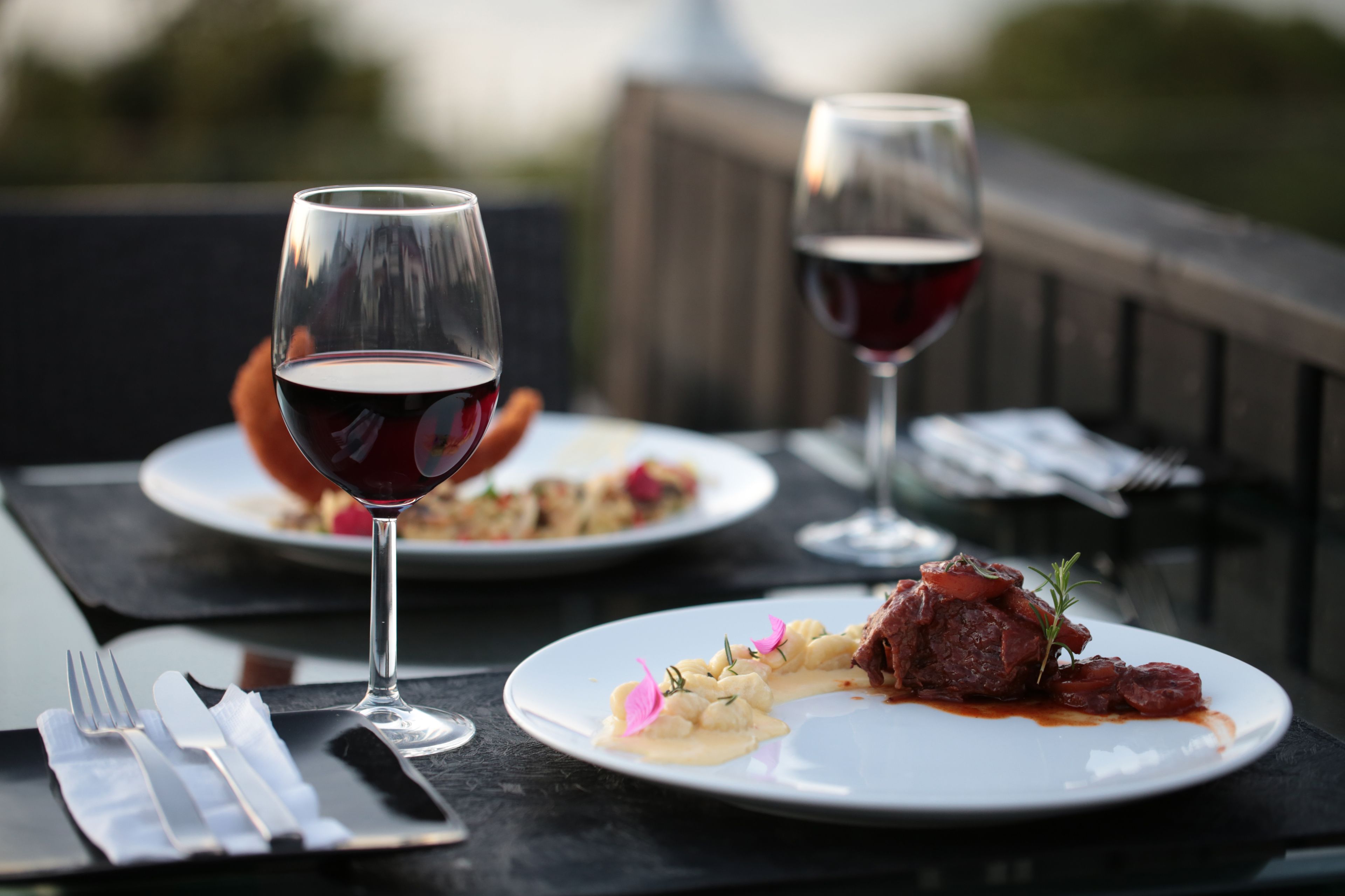 Una mesa de comedor con dos platos de comida, dos copas de vino y cubiertos.