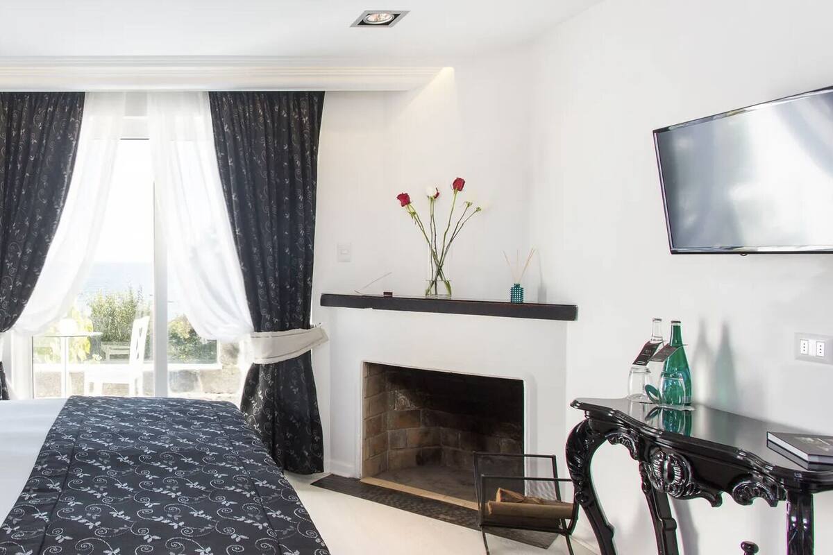 A modern bedroom with a large bed, a fireplace, and a balcony with curtains.
