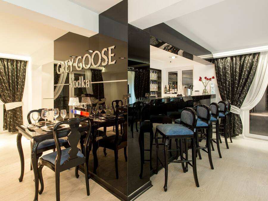 A dining area with a bar, dark wooden chairs, and a glass partition with 'GREY GOOSE' branding.