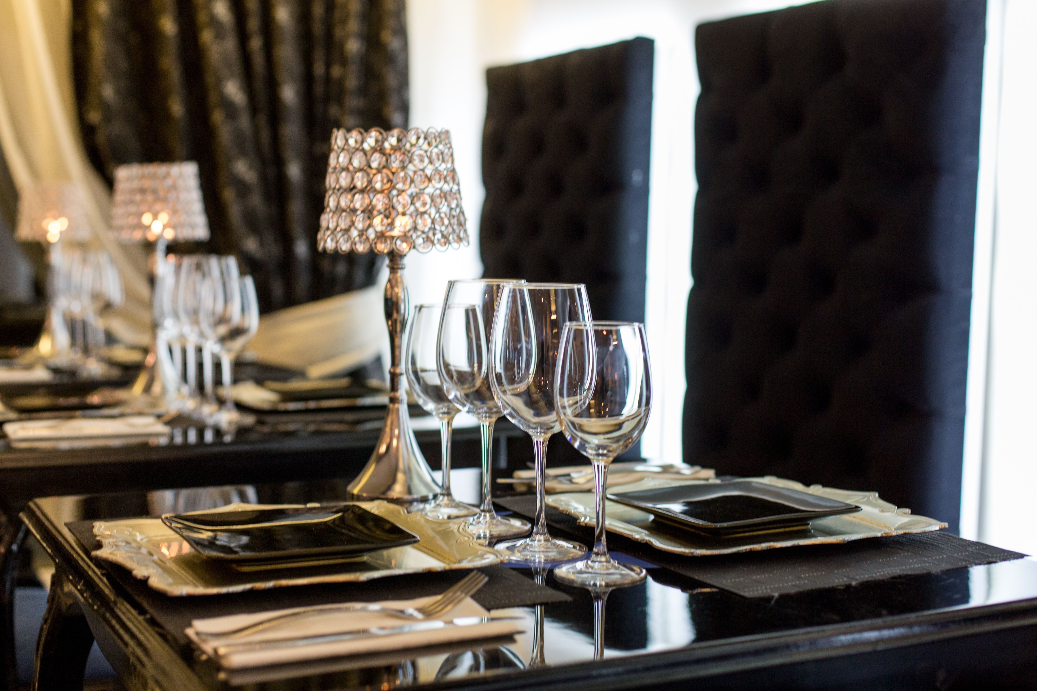 A dining table set with wine glasses, plates, cutlery, and a decorative lamp.