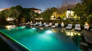 Una piscina con sillas de descanso y un pequeño edificio con luces.