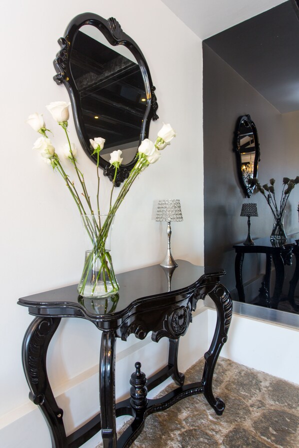 A black ornate console table with a vase of white flowers and a lamp.