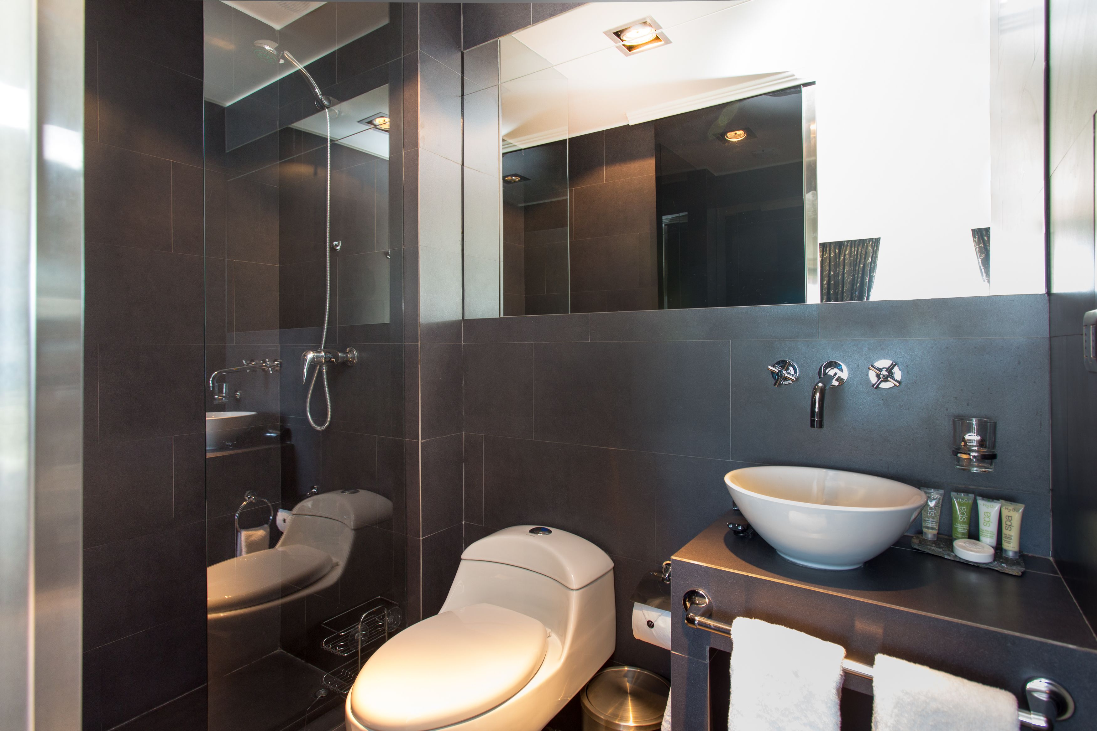 Et moderne badeværelse med en glasafskærmet bruser, toilet, vask med stor kumme og et spejl over vasken.