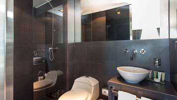 Et moderne badeværelse med en glasafskærmet bruser, toilet, vask med stor kumme og et spejl over vasken.