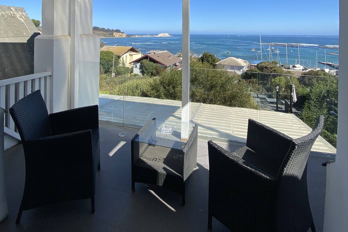 A covered outdoor seating area with a view of the sea and boats.