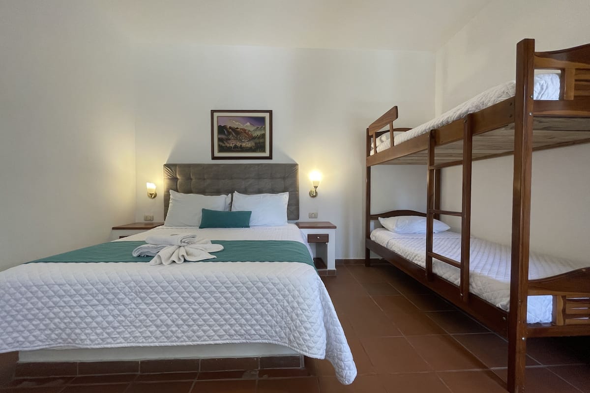 A single bed with a quilted white duvet, a wooden headboard, and a bedside table with a lamp. There is a bunk bed to the right.