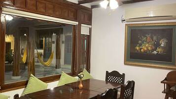 A dining area with a wooden table and chairs, a large window with a view of the outside, and a ceiling fan.