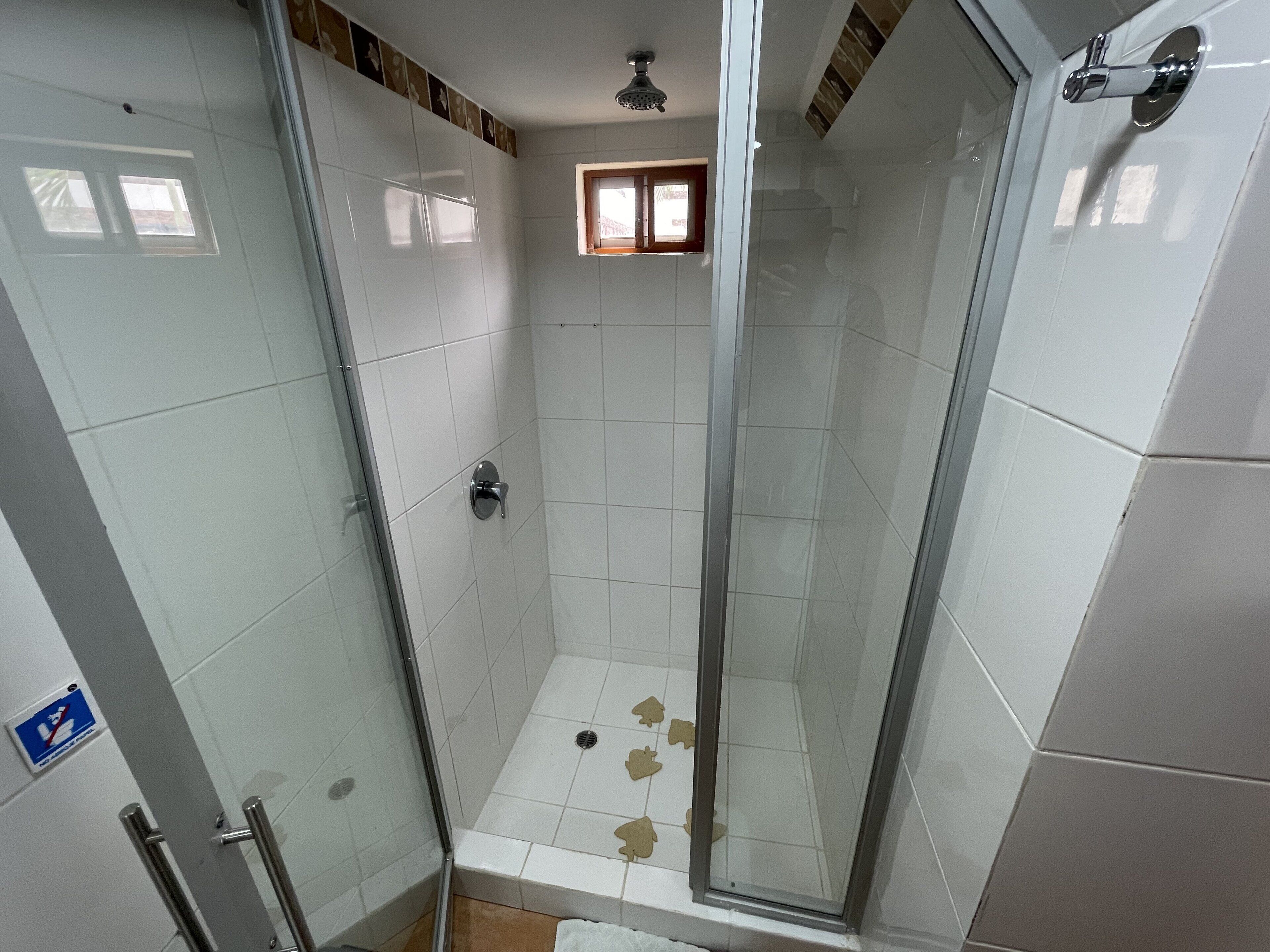 A glass-enclosed shower with white tiles, a small window, and a visible drain.