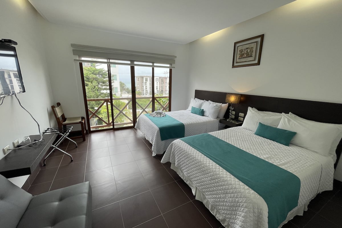 A hotel room with two beds, a desk, and a chair.