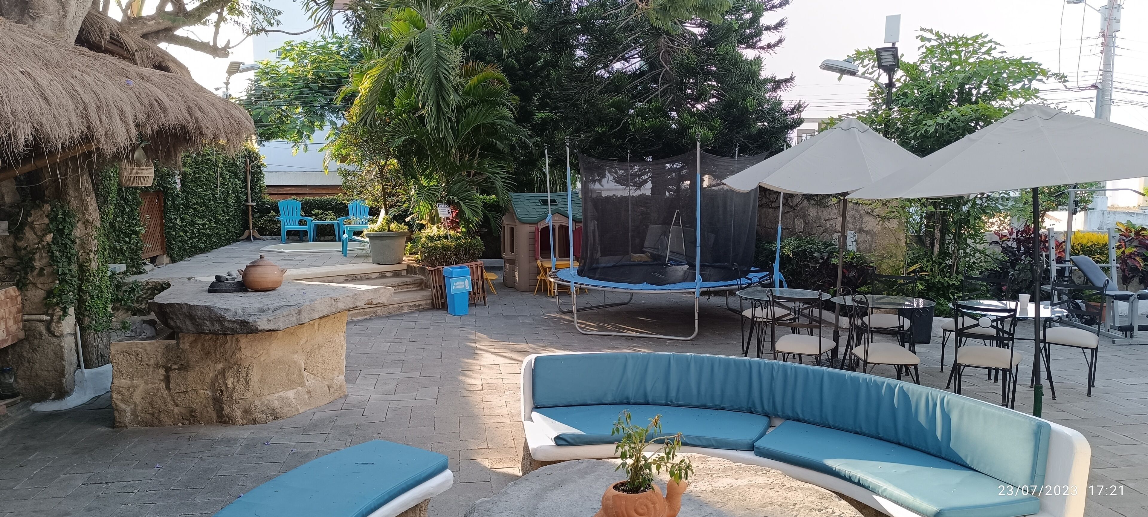 An outdoor patio with a stone bench, a swing, a trampoline, and a seating area with a curved blue sofa.