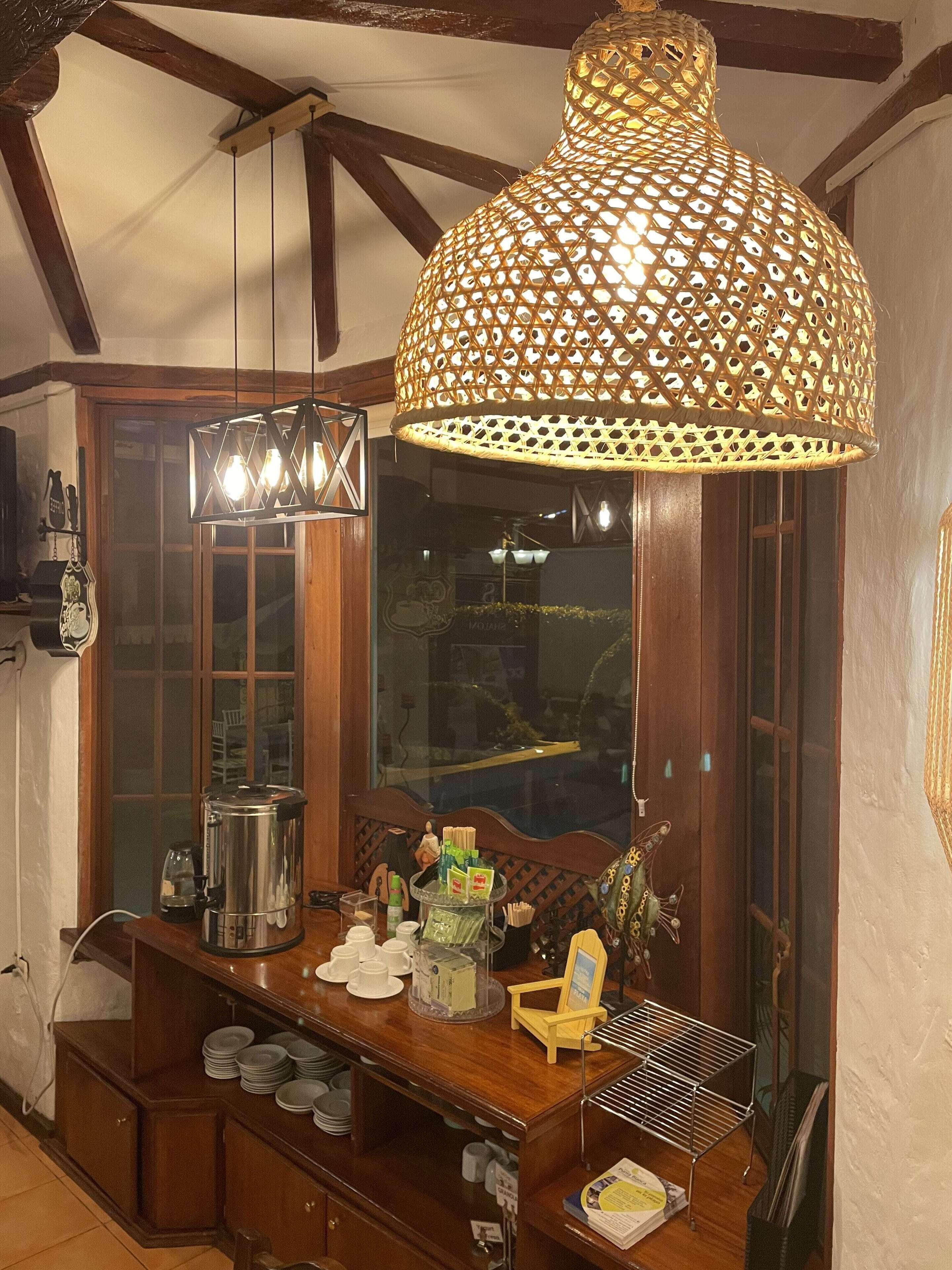 A wooden bar area with a large woven light fixture, a coffee machine, and various barware.