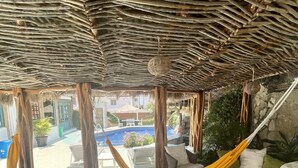 Un área de descanso al aire libre con techo de tejido, una hamaca y una piscina al fondo.